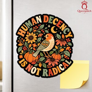 Könnte beinhalten: Ein runder Magnet mit einer zentralen Abbildung eines Vogels, umgeben von Sonnenblumen, Kürbissen und Blattwerk. Der Text "HUMAN DECENCY IS NOT RADICAL" ist in einer fetten, geschwungenen Schriftart entlang des Randes aufgedruckt.