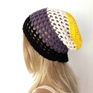 Puede incluir: Un gorro de punto de ganchillo con un esquema de color negro, morado, blanco y amarillo. El gorro está hecho con un punto de malla.