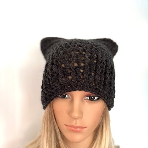 May include: A black knitted beanie with a loose, open weave pattern. The beanie is worn on a mannequin with blonde hair.