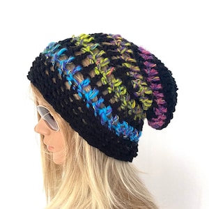 Op de afbeelding: Een zwarte gehaakte beanie met een kleurrijk gestreept patroon. De strepen zijn groen, blauw, paars en zwart.