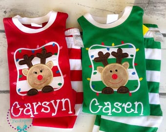May include: Two sets of children's Christmas pajamas. One set is red with white and red striped pants, the other is green with white and green striped pants. Each top features a reindeer design with the name "Garsyn" and "Casen".