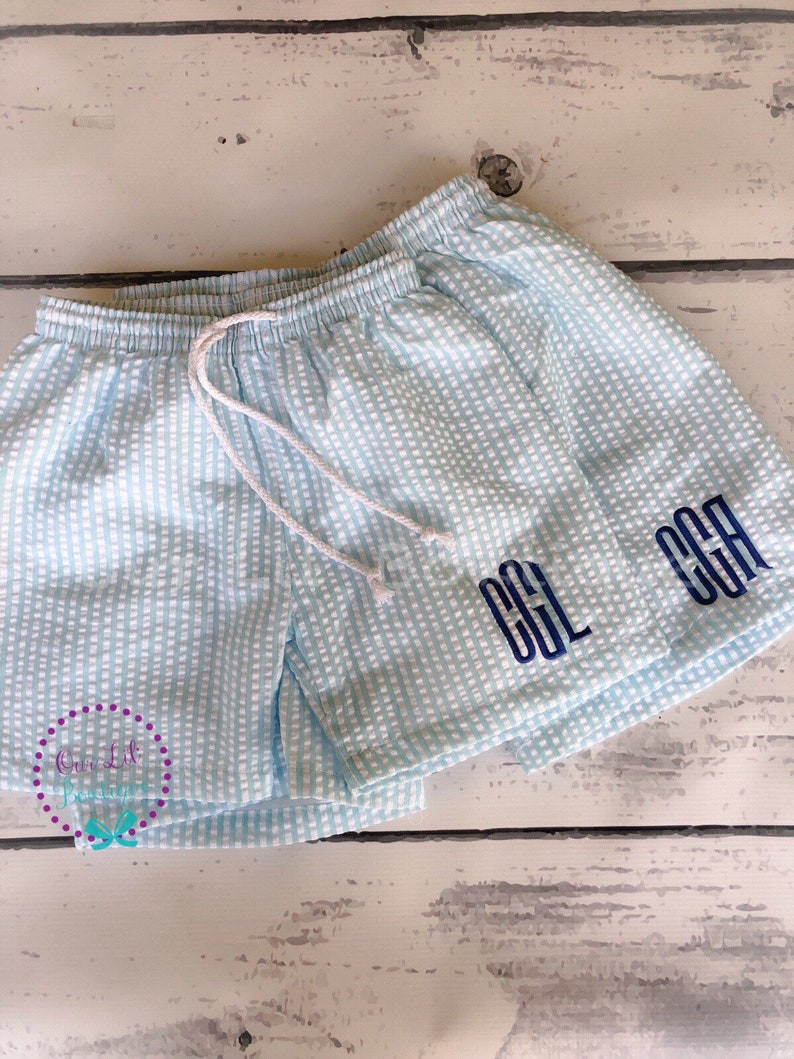 Puede incluir: Pantalones cortos de seersucker en azul claro y blanco con cintura el&aacute;stica y cord&oacute;n blanco. Los pantalones est&aacute;n bordados con las letras de monograma azul oscuro CGL en la pierna derecha. La tela presenta un patr&oacute;n de rayas texturizado.