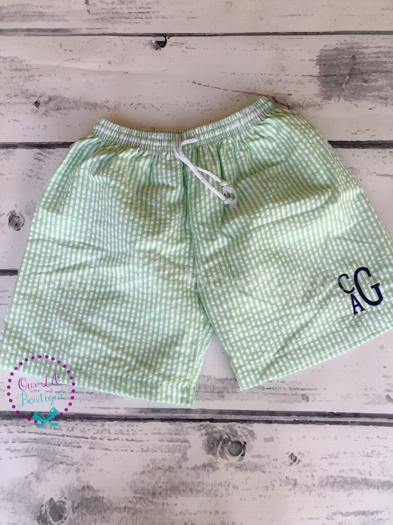 Puede incluir: Pantalones cortos de seersucker con estampado de cuadros vichy en verde claro y blanco, con cintura el&aacute;stica y cord&oacute;n blanco. La pierna derecha inferior muestra un monograma bordado en azul marino oscuro con las letras CAG en tipograf&iacute;a serif.