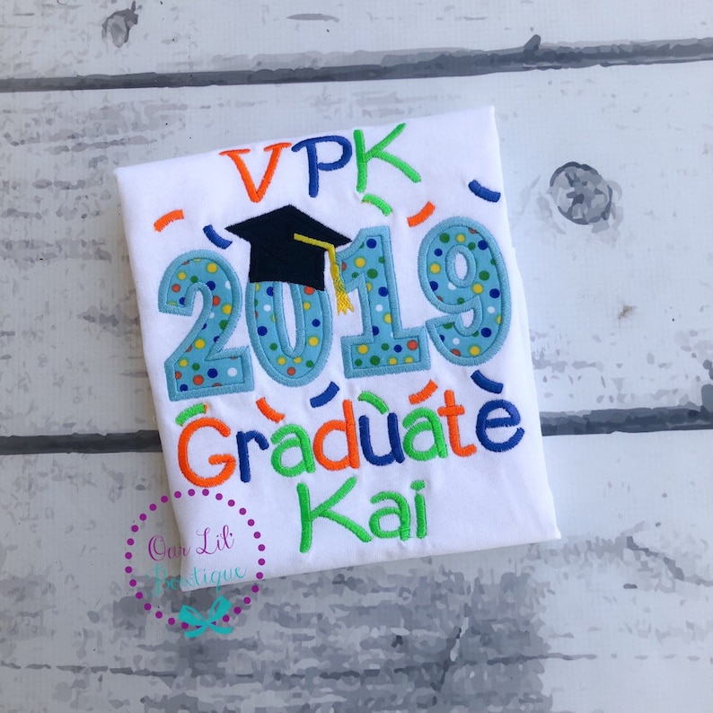 May include: White t-shirt with blue, orange, and green embroidered text that reads "VPK 2019 Graduate Kai". A black graduation cap is embroidered above the year 2019.