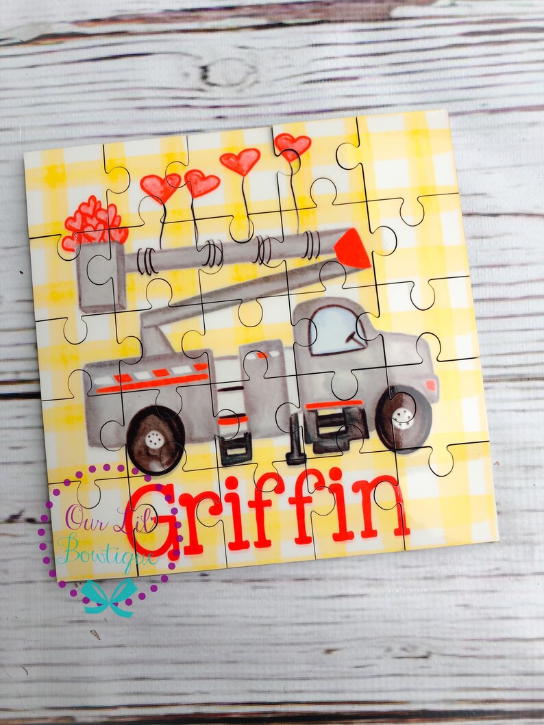 Puede incluir: Un rompecabezas personalizado con un cami&oacute;n gris con detalles rojos y globos en forma de coraz&oacute;n. El nombre "Griffin" est&aacute; impreso en rojo. El rompecabezas tiene un fondo de cuadros amarillos y est&aacute; hecho de varias piezas.