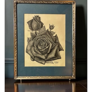 May include: A framed ink drawing on cream paper featuring a large, detailed rose in full bloom with a smaller rosebud above it. The artwork is encased in a dark teal mat and an ornate, textured gold-toned metal frame with a signature in the corner.