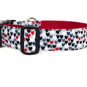 May include: A grey dog collar with a red, white, and black heart pattern. The collar has a black buckle and a red lining.