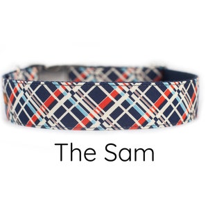 May include: A navy blue dog collar with a white, red, and blue plaid pattern. The text "The Sam" is printed below the collar.
