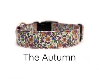 May include: A dog collar with a floral pattern in shades of brown, purple, blue, and green on a white background. The collar has a black buckle and a silver metal ring. The text "The Autumn" is below the collar.