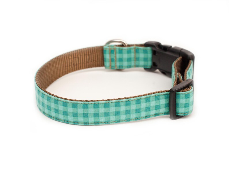 May include: A teal and brown dog collar with a checkered pattern and a black plastic buckle.