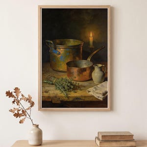 May include: A framed wall art print depicting a still life scene with a large copper pot, a smaller copper saucepan, a ceramic pitcher, a bundle of green herbs, and a folded cloth on a wooden table, illuminated by a single lit candle.