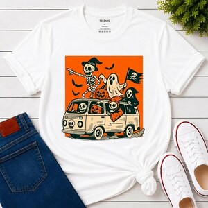 May include: A white short-sleeve t-shirt featuring a graphic print of a vintage van on an orange background. The van is filled with cartoon skeletons, ghosts, and jack-o'-lanterns. The text TEEZANO is printed on the inside neck label.