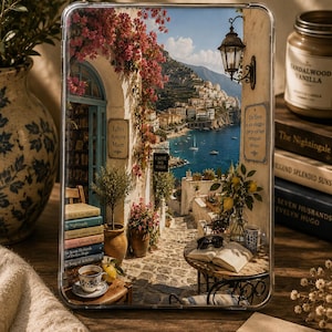 Op de afbeelding: Een doorzichtige tablethoes met een bedrukte illustratie van een Italiaans kustdorp, een boekhandel, bloeiende roze bougainville, een stenen pad, een cafétafel met een open boek en de tekst Libri Amore Mare en Caffe del Mare.