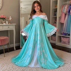 May include: A floor-length turquoise dress with an off-the-shoulder white neckline, long flared sleeves with white lace trim, and a white underskirt. The turquoise fabric features a repeating pattern of silver stars and a front center slit.