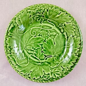 Puede incluir: Un plato de cerámica verde con un diseño de hojas en relieve. El plato presenta un patrón detallado de hojas y vides, con un borde texturizado. El plato es redondo y tiene un acabado brillante, ideal para servir alimentos.