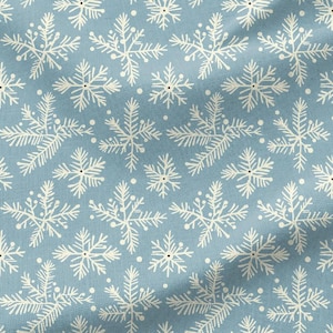 Könnte beinhalten: Ein hellblauer Stoff mit einem sich wiederholenden Muster aus weißen, astartigen Schneeflocken. Das Textil weist eine sichtbare Webstruktur auf, wobei kleine weiße Punkte zwischen den größeren, symmetrischen, sechsstrahligen Formen liegen.