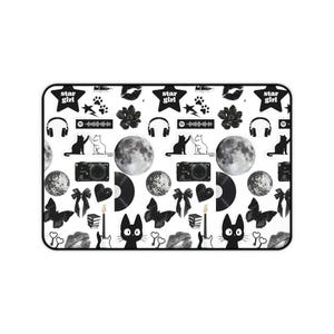 Puede incluir: Una alfombrilla de escritorio rectangular con un patrón repetitivo en blanco y negro de varios iconos, incluyendo estrellas con el texto star girl, auriculares, lunas, bolas de discoteca, cámaras, guitarras, mariposas y gatos.