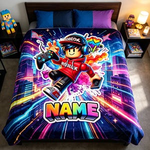May include: A plush blanket featuring a vibrant Roblox-themed graphic of a character wearing a red hoodie, headphones, and a cap, holding a game controller. The design includes a neon city background, colourful light streaks, and the word NAME in block letters.