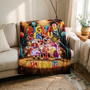 May include: A rectangular throw blanket featuring a colourful circus-themed graphic with the text THE AMAZING DIGITAL CIRCUS and NAME. The design includes multiple cartoon characters, yellow stars, and balloons against a stage curtain background.