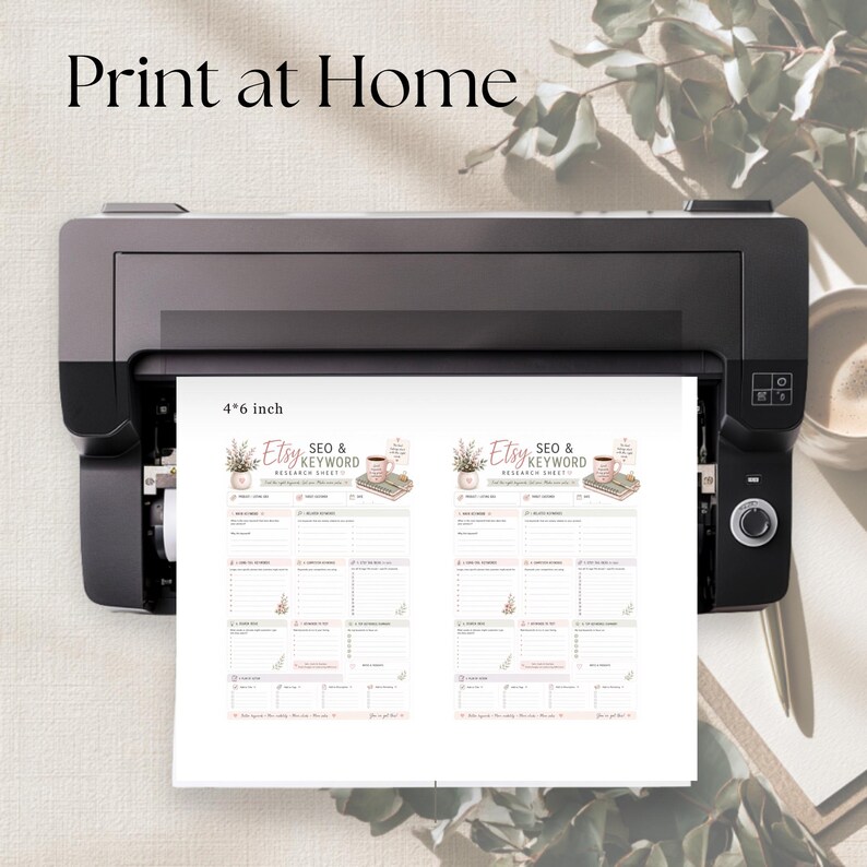 May include: A black printer outputting a white sheet of paper with two identical copies of an Etsy SEO and keyword research sheet. The document features floral graphics, a mug, and text labels. The paper is clearly marked with 4x6 inch dimensions.