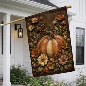 May include: A rectangular garden flag featuring a central orange pumpkin surrounded by a dense arrangement of autumn-toned flowers and foliage. The design is set against a dark brown textured background, creating a layered, dimensional appearance.