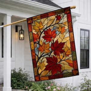 May include: A rectangular garden flag featuring a stained glass style design of autumn maple leaves in shades of red, orange, and yellow. The leaves are arranged on branches against a light background, framed by a border of dark red and brown squares.