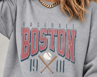 May include: A heather gray crewneck sweatshirt featuring a graphic print with the text BASEBALL BOSTON 19 01. The design includes large red block letters for BOSTON, a white baseball, and two crossed brown wooden baseball bats.