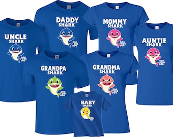 May include: A collection of seven royal blue t-shirts featuring cartoon shark illustrations and white text. Each shirt displays a specific family role including Daddy, Mommy, Uncle, Auntie, Grandpa, Grandma, and Baby Shark, accompanied by the text Doo Doo Doo.