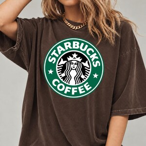 May include: A dark brown, short-sleeved t-shirt featuring the green and white Starbucks Coffee circular logo printed on the center of the chest. The garment has a relaxed, loose fit with a crew neckline and a slightly faded, vintage-style fabric texture.