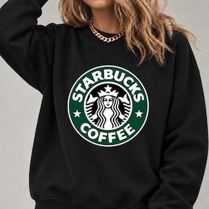 May include: A black long-sleeve crewneck sweatshirt featuring a large, circular green and white Starbucks Coffee logo graphic on the chest. The logo includes the iconic siren illustration, the text Starbucks Coffee, and two small stars.