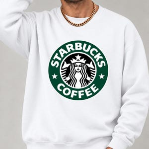 May include: A white long-sleeve crewneck sweatshirt featuring the green and white Starbucks Coffee circular logo printed on the center of the chest. The garment has ribbed cuffs and a ribbed hem, providing a clean and simple look.