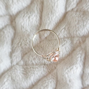 May include: A delicate silver ring with a pink gemstone wrapped in wire.