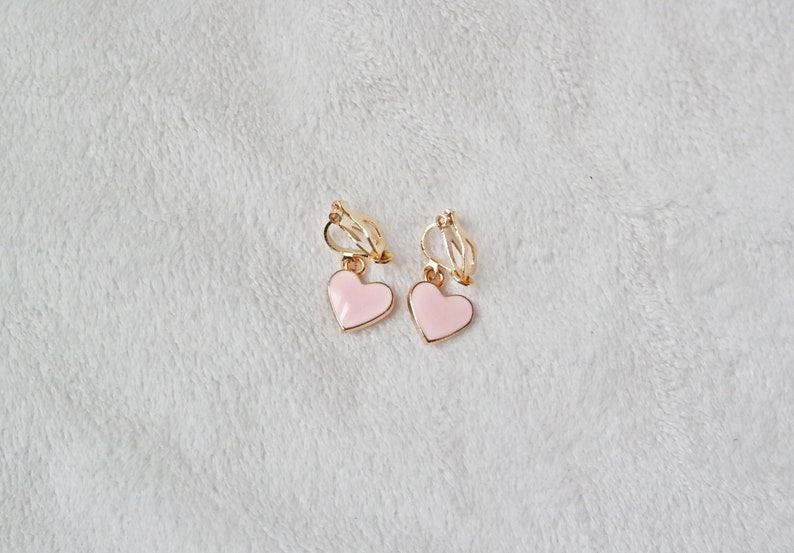 May include: A pair of gold clip-on earrings with pink heart-shaped charms.