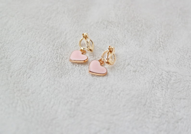 May include: A pair of gold clip-on earrings with pink heart-shaped charms.