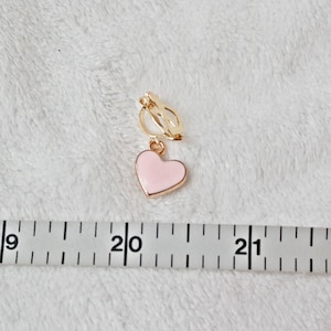 May include: A gold heart-shaped clip-on earring with a pink enamel heart charm. The earring is approximately 2 inches long.
