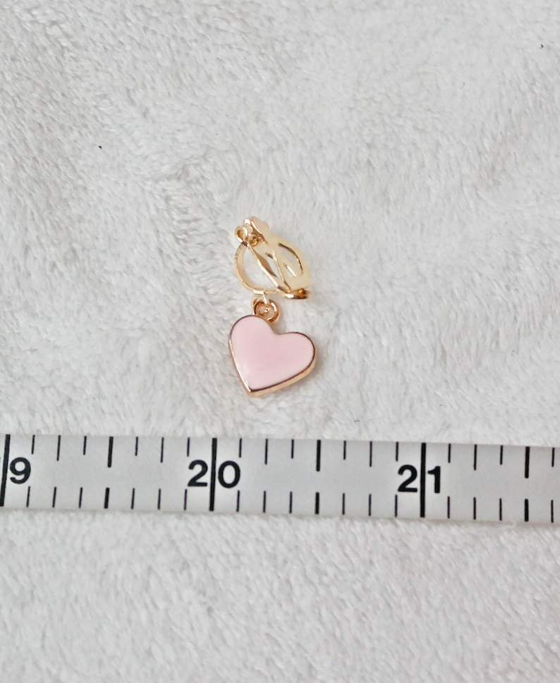 May include: A gold heart-shaped clip-on earring with a pink enamel heart charm. The earring is approximately 2 inches long.