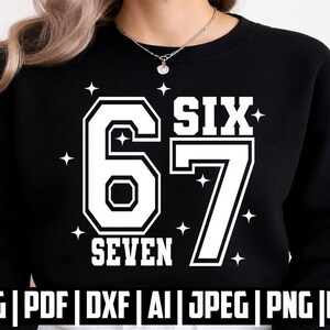 May include: A black long-sleeve sweatshirt featuring a large white graphic print of the number 67 with the words SIX and SEVEN printed in a bold block font. The design is accented with small four-pointed star shapes surrounding the numbers.