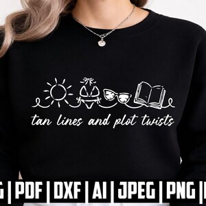 Pode incluir: Uma camisola preta de gola redonda com um design gráfico branco de um sol, um biquíni, óculos de sol e um livro aberto, com o texto "tan lines and plot twists" impresso abaixo dos ícones numa fonte cursiva branca.