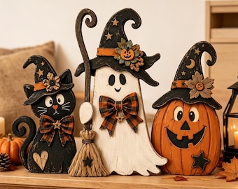 Puede incluir: Un conjunto de tres decoraciones de Halloween de madera que incluye un gato negro, un fantasma blanco y una calabaza naranja. Cada figura lleva un sombrero de bruja negro adornado con estrellas, flores y lazos de cuadros, y un escobón.