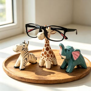 May include: A set of three carved wooden animal figurines including a zebra with black stripes, a giraffe with brown spots, and a teal elephant with pink ears. The giraffe figurine supports a pair of black-framed eyeglasses on its head.