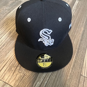 May include: A black New Era 59FIFTY fitted baseball cap featuring a white embroidered Chicago White Sox logo on the front, white eyelets, and a circular sticker on the flat brim displaying the size 7 1/2, which corresponds to 59.6 cm.