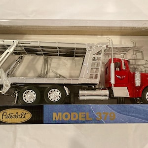 May include: A red and silver Peterbilt Model 379 die-cast toy lorry with a car transporter trailer, packaged in a rectangular box labelled LongHauler collection and Model 379, featuring chrome-coloured details, black wheels, and a warning label.