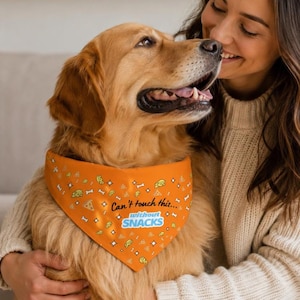 May include: An orange pet bandana featuring a repeating pattern of small pizza slices, cheese wedges, and bones, with the text Can't touch this... without SNACKS printed in black and blue lettering across the center of the fabric accessory.