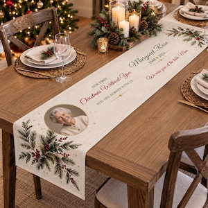 Könnte beinhalten: Ein cremefarbener Tischläufer aus Stoff mit einem kreisförmigen Foto einer älteren Frau, grünen Tannenzweigen mit roten Beeren und dem Text: Our First Christmas Without You, Margaret Rose 1948-2026, You Are Always With Us, We miss you at the table, Mom.
