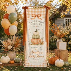 May include: A vertical banner with a light orange gingham pattern featuring a stack of three pumpkins, a bow graphic, and the text A Little Pumpkin Is On the Way, Welcome To Amelia's Baby Shower, and the date November 16, 2026, tied with orange ribbons.