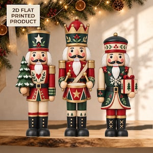 May include: Three nutcracker figures in red, green, and gold. The left figure holds a tree, the centre plays a drum, and the right holds a gift. Each wears a uniform with painted details and a white beard. Text reads: 2D FLAT PRINTED PRODUCT.