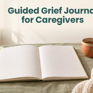 May include: An open journal with lined pages and rectangular boxes at the top and bottom of each page. The text Guided Grief Journal for Caregivers is displayed above the book. A brown ceramic mug and a cream-coloured knit fabric are nearby.
