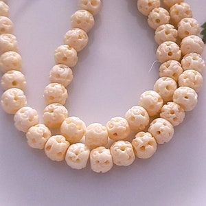 May include: A strand of white carved bone beads with intricate designs. The beads are strung on a white cord and are arranged in a circular pattern.