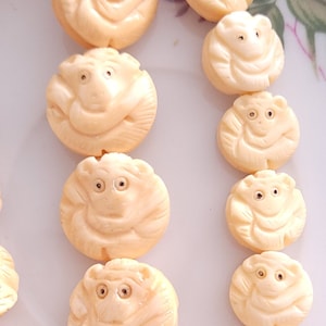 May include: A strand of ivory beads with carved monkey faces. The beads are round and have a creamy white color.