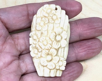 May include: A carved ivory pendant with a floral design. The pendant is oval shaped and has a hole at the top for hanging.